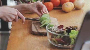 Young and happy woman eating healthy salad sitting on the table with green fresh ingredients indoors video