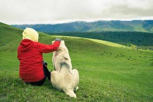 hembra mujer caminante sentado con grande perro al aire libre en montañas naturaleza. persona caricias perro. joven niña gasto hora con perro en ocio foto