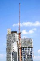 Building under construction with hoisting cranes on bright blue sky background photo