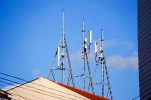 Look up view of communication tower with antennas on the top of building and bright blue sky background. photo