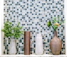 Ornamental plants in different vases put on white shelf front of square pattern tile in the toilet.