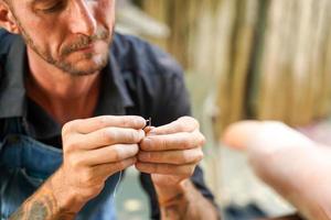 Closeup and crop leather craftsman is carefully threading a needle to sew a leather product for a customer. photo