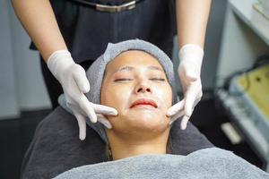 Closeup beauty woman making face spa and facial mask from cream to condition and treat the face in beauty clinic. photo