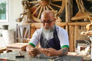 Closeup Asian man leather product maker looking at pieces leather skins to make products in his shop. photo