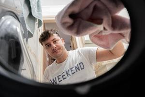 Man view from washing machine inside. Male does laundry daily routine. photo