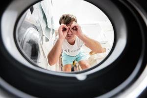 Man view from washing machine inside. Male does laundry daily routine. Looking through binoculars gesture. photo