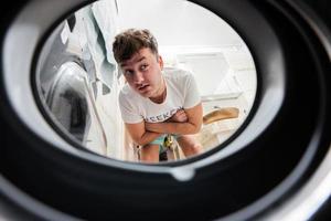 Man view from washing machine inside. Male does laundry daily routine. Waits for the washing to finish. photo