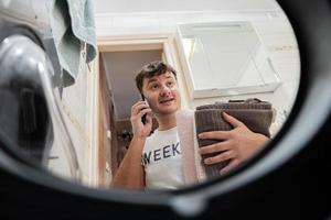 Man view from washing machine inside, speaking by phone with wife. Male does laundry daily routine. photo