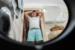 hombre ver desde Lavado máquina adentro. masculino lo hace lavandería diario rutina. poner su manos en cabeza en frustración. foto