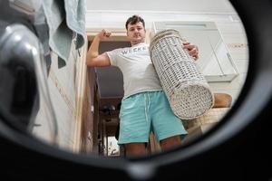 Man with basket, view from washing machine inside. Male does laundry daily routine. Show his muscle. photo