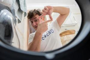 Man view from washing machine inside. Male does laundry daily routine. Made a photo frame with fingers.