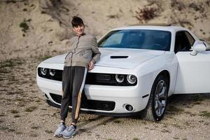 Teenager boy stand near white muscle car. Young teen driver. photo