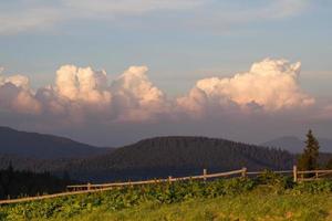 Carpathian mountains and fluffy evening clouds over fence landscape photo