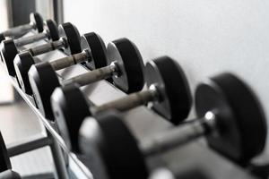 pararse con pesas. Sala de deportes y fitness. equipo de entrenamiento con pesas. juego de mancuernas negras, muchas mancuernas en el rack en el gimnasio deportivo foto