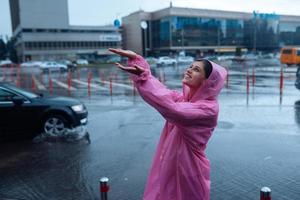 joven mujer sonriente con un impermeable rosa disfrutando de un día lluvioso. foto