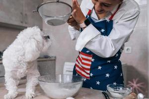 Woman in the kitchen sifts flour together with a dog photo