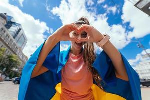 Young woman with Ukrainian flag shows heart with hands photo
