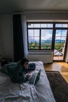 Young woman working on laptop while lying on bed photo