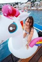 Happy young woman sitting on inflatable unicorn toy mattress photo