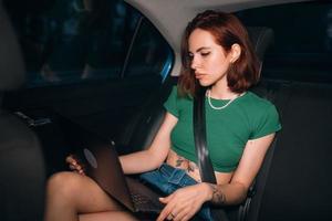 Beautiful woman is using laptop while sitting on back seat photo
