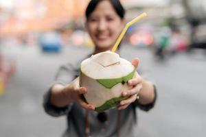 Happy young Asian woman backpack traveler drinking a coconut juice at China town street food market in Bangkok, Thailand. Traveler checking out side streets. photo