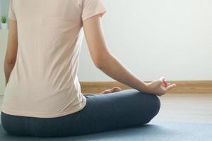 The back of an attractive asian woman in sportswear sitting in a lotus position while doing yoga in the room. photo