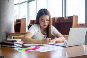 hembra estudiantes sentar y hacer deberes tomar notas, hacer informes en el biblioteca. foto