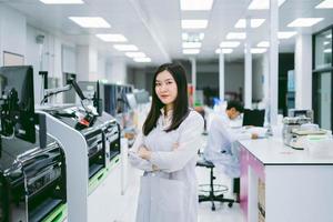 young smiling scientist in white lab coat standing with automation blood analyzer at medical laboratory photo