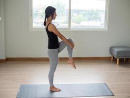 The women exercise by lifting the legs, knees up one by one, holding the knees tightly. Stand straight back and hold. Is a relaxing yoga practice at home. photo