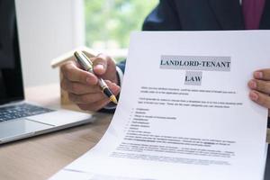 The hand of a man holding a house purchase contract with a pen showing up to customers. House salesman is showing Landlord-Tenant Law document. photo