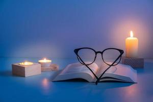 Eyes glasses and Holy Bible with candles lighting on blue background. Variative focus
