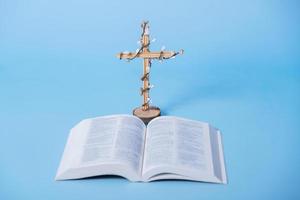 Cross decorated flowers with Holy Bible on blue background. Easter holiday minimalistic concept photo