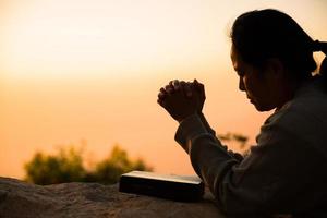 Silhouette of woman kneeling down praying for worship God at sky background. Christians pray to jesus christ for calmness. In morning people got to a quiet place and prayed. copy space. photo