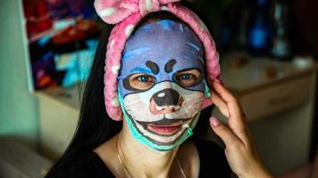 Young girl with facial mask looking at camera over interior background. Cosmetic procedure. Beauty spa and cosmetology. photo