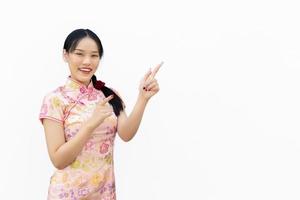 Asian woman with long hair who wears pink Cheongsam dress in Chinese new year theme while her hand shows to present something and showing hand to point smiling happily isolated on white background. photo