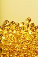 Pile of golden capsules of vitamin D3 on a yellow background with free space photo