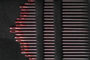 agujas de coser de diferentes tamaños en un conjunto de rojo sobre fondo negro. foto