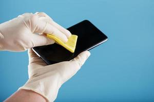 Cleaning a smartphone with a sterile yellow napkin in rubber gloves on a blue background. photo