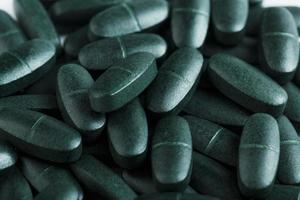 Spirulina pills are green in color with multivitamins in full screen as a background photo