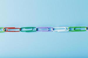 Interlocked colored paper clips in a line on a blue background with free space photo