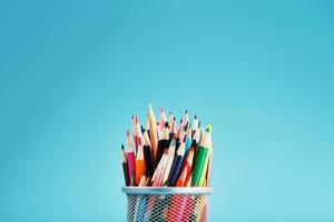 Pencils of different colors in a glass on a blue background. photo