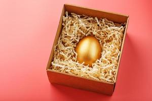 Egg made of gold in a wooden box on a pink background. The concept of exclusivity and superprize. Minimalistic composition. photo