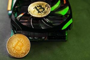 en los poderosos ventiladores de la tarjeta de video hay monedas de la criptomoneda bitcoin con una luz de fondo verde foto