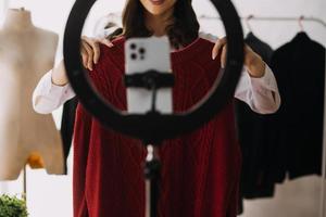 Beautiful lady blogger showing clothes in front of the camera to recording vlog video live streaming at her shop. Online Shopping Cart notion. photo