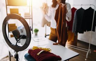 hermosa dama blogger demostración ropa en frente de el cámara a grabación vlog vídeo En Vivo transmisión a su tienda. en línea compras carro noción. foto