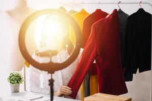 Beautiful lady blogger showing clothes in front of the camera to recording vlog video live streaming at her shop. Online Shopping Cart notion. photo