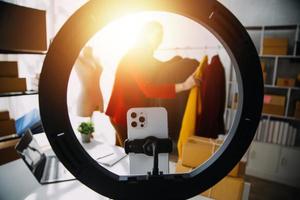 Beautiful lady blogger showing clothes in front of the camera to recording vlog video live streaming at her shop. Online Shopping Cart notion. photo