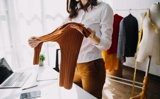 Beautiful lady blogger showing clothes in front of the camera to recording vlog video live streaming at her shop. Online Shopping Cart notion. photo