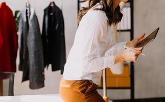Beautiful lady blogger showing clothes in front of the camera to recording vlog video live streaming at her shop. Online Shopping Cart notion. photo