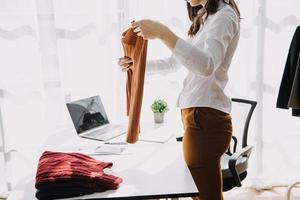 Beautiful lady blogger showing clothes in front of the camera to recording vlog video live streaming at her shop. Online Shopping Cart notion. photo